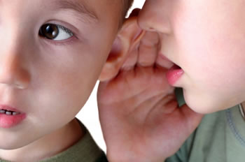 Young boy listening to a friend talking into his hear, demonstrating symptoms of Auditory Processing Disorder.