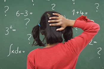 Young femaile student having difficulty with math problem on chalkboard displaying symptoms of Dyscalculia.