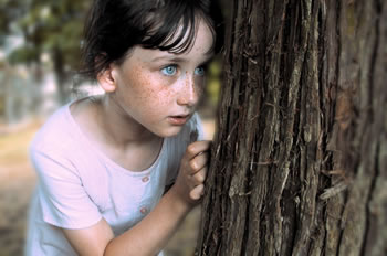 Young girl hiding behind tree isolated from classmates or friends