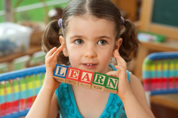 Little girl holding up toy blocks that spell "LEARN".