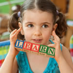 Little girl holding up toy blocks that spell "LEARN".