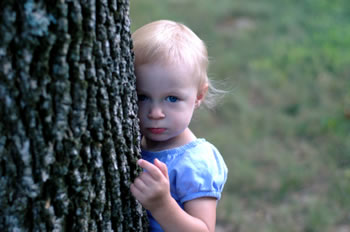 Little girl standing behind a tree